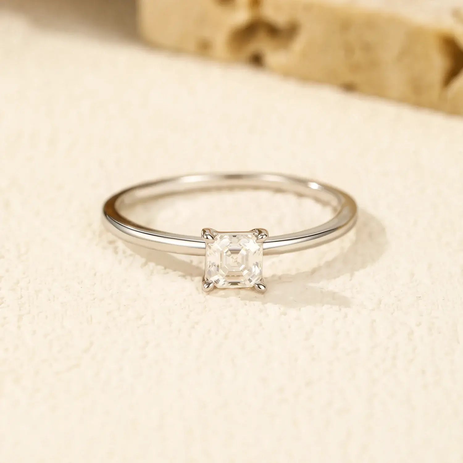 Emerald Cut Moissanite Ring on a soft textured surface, featuring a sparkling 0.35CT moissanite in a classic prong setting.