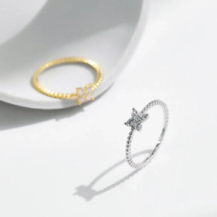 Four Leaf Clover Moissanite Ring 925 Sterling Silver next to a gold ring on a minimalist background.