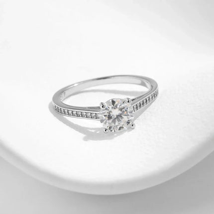 Lab Diamond 1CT Moissanite Ring set on a smooth surface, featuring a round moissanite surrounded by zircon side stones.