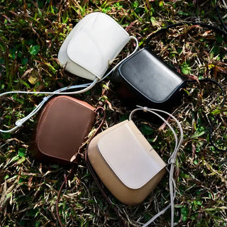 Leather shoulder bags in white, black, brown, and beige on grass, elegantly stylish and versatile for various occasions.