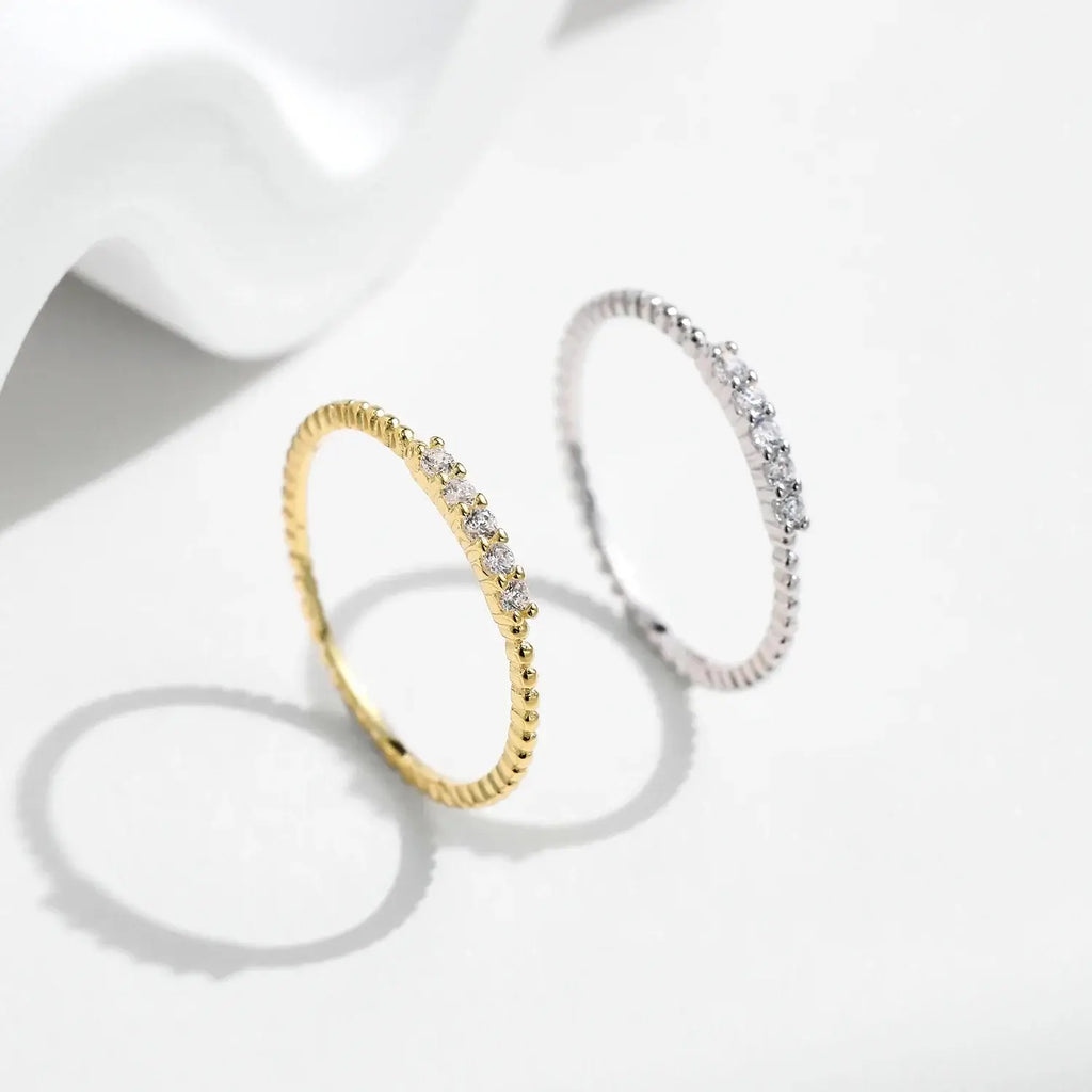 Moissanite Eternity Band Ring in 925 Sterling Silver displayed alongside a gold ring with multiple sparkling stones.