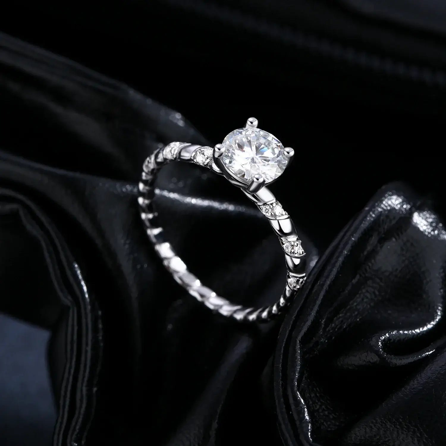 Moissanite Twist Ring in 925 Sterling Silver on a black satin background, showcasing a brilliant round-cut moissanite.