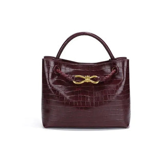 Women's Handbag in burgundy croc pattern with gold bow detail and soft structure.