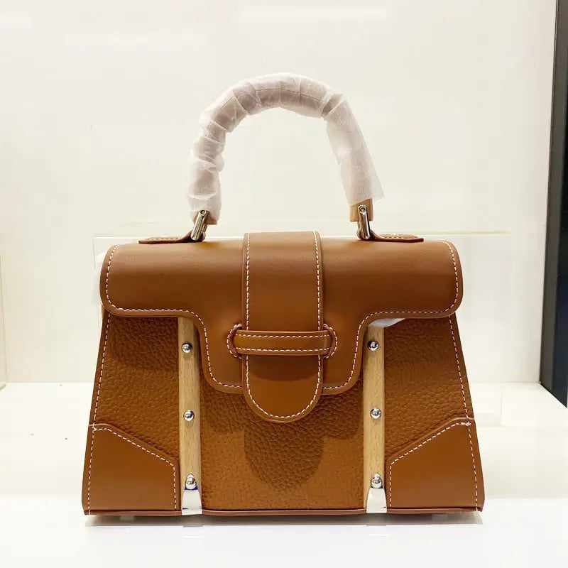 Handbag with wooden handle and rivet decoration, featuring a cover closure, designed for women.