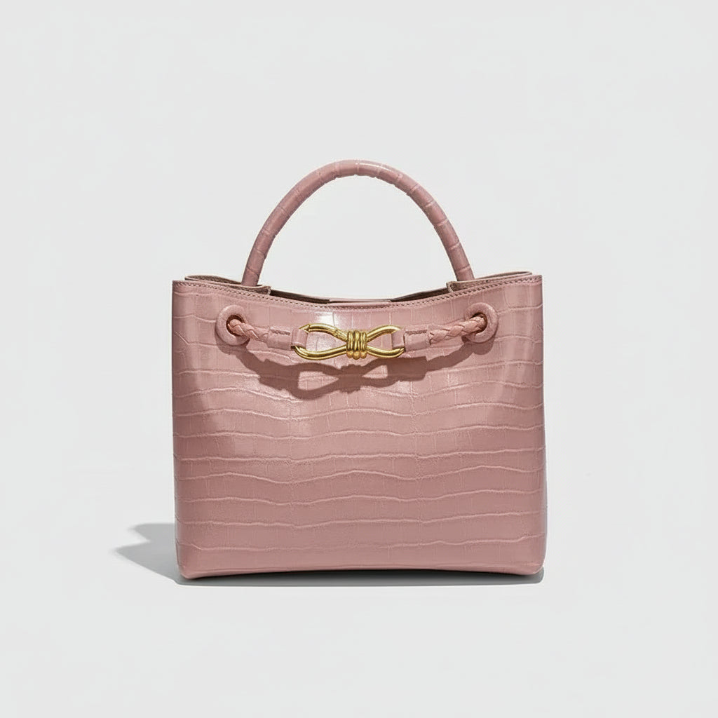 Women's Handbag in soft pink crocodile pattern with gold bow closure.
