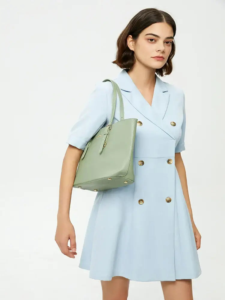 Model wearing a light blue dress with buttons, carrying a green tote bag with adjustable shoulder straps.