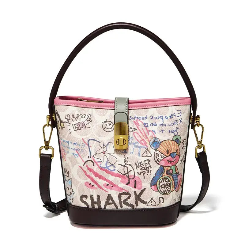 Trendy graffiti print bucket bag for women, soft PU leather, pink and beige, with top handle and crossbody strap.