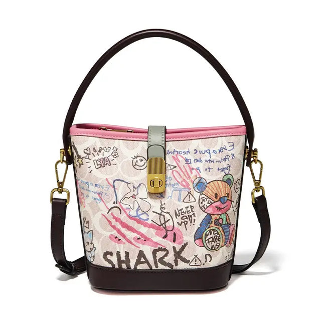 Trendy graffiti print bucket bag for women, soft PU leather, pink and beige, with top handle and crossbody strap.