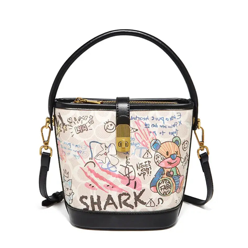 Trendy women's graffiti print bucket bag in white with black accents and top handle, perfect for casual outings.
