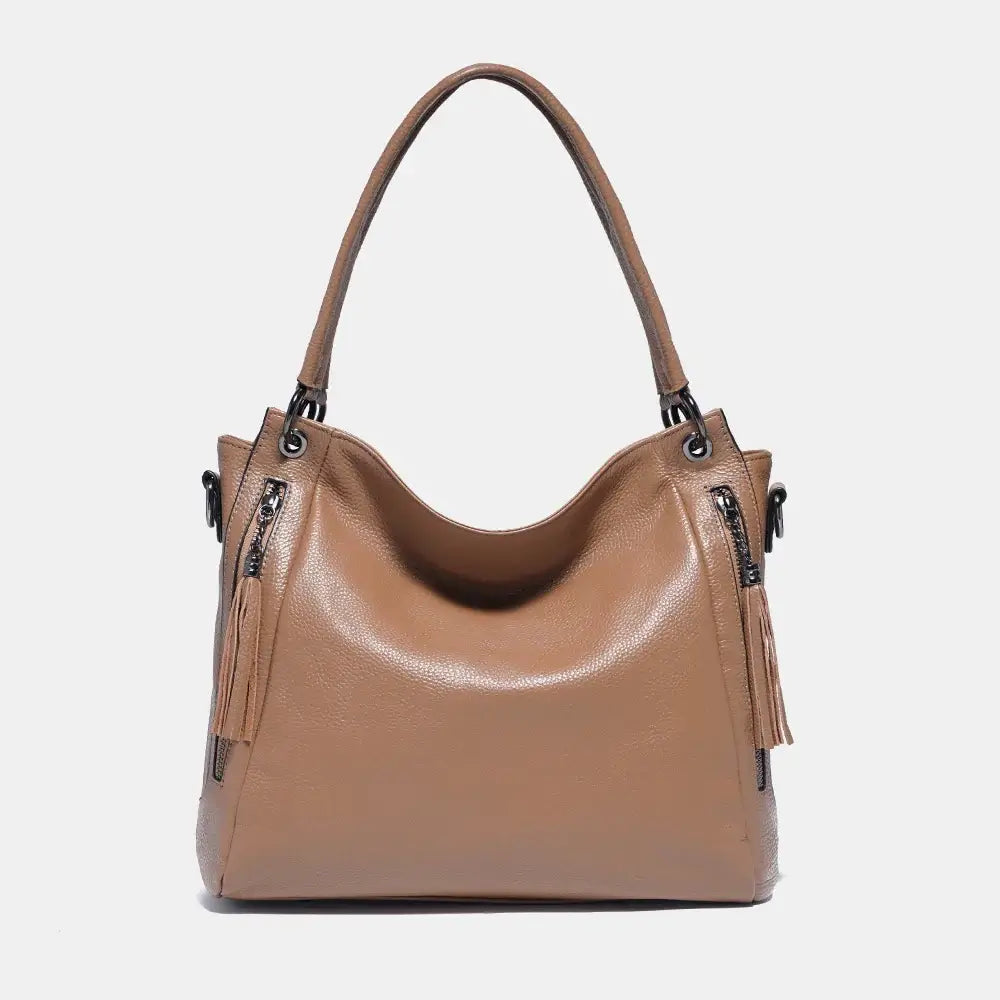 Shoulder hobo bag in tan leather with tassel detail, spacious design, and multiple carrying options for stylish women.