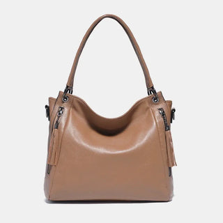 Shoulder hobo bag in tan leather with tassel detail, spacious design, and multiple carrying options for stylish women.