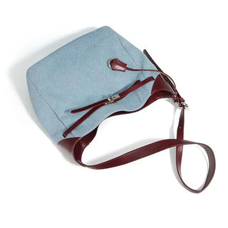 Casual women’s shoulder bag in light blue denim with brown leather strap, trendy bucket tote design.